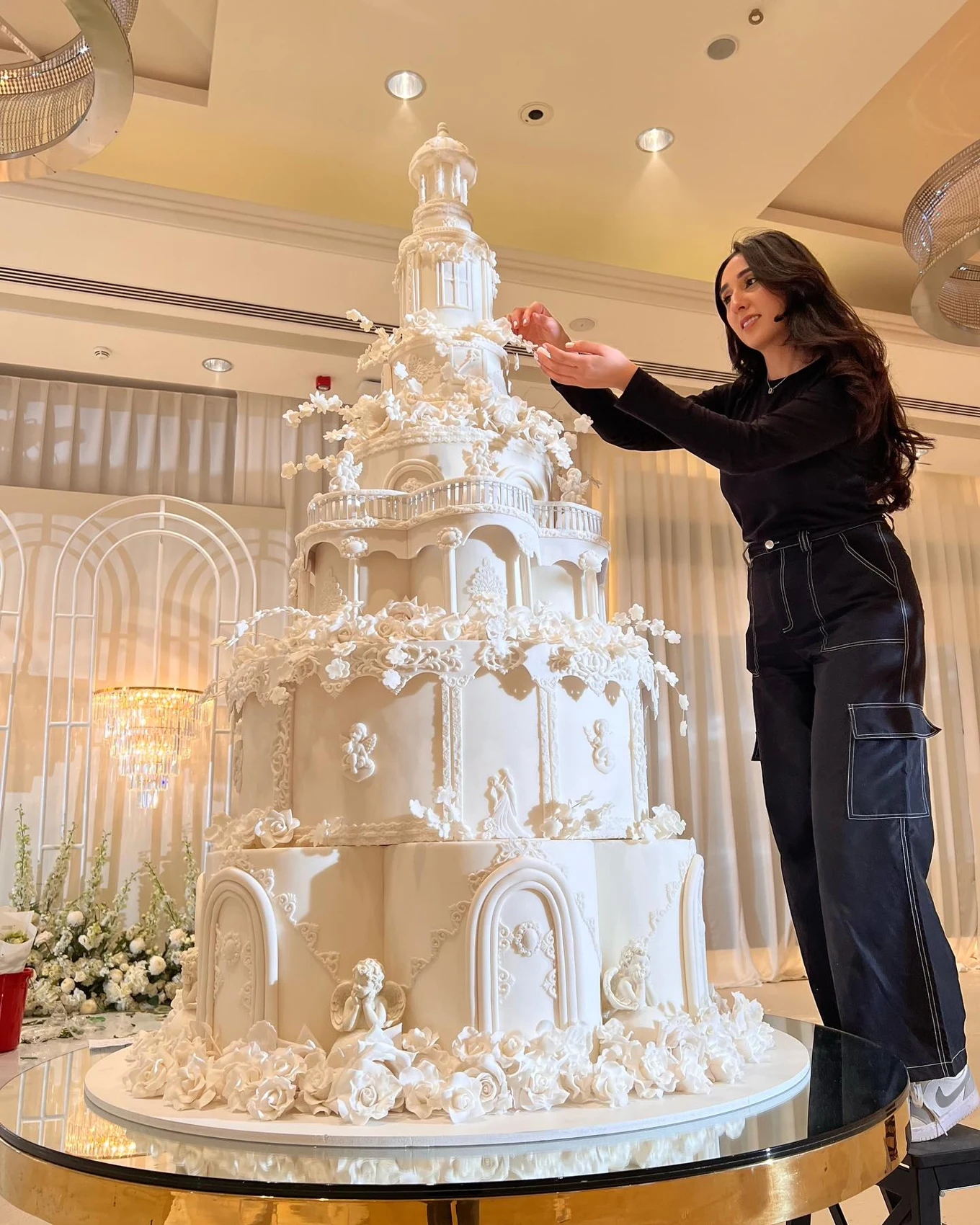 Zoya arranging delicate sugar flowers on a grand white wedding cake